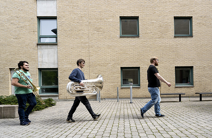 Tre personer med instrument går utanför en tegelbyggnad