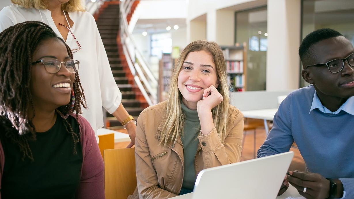 Tre studenter tillsammans med en lärare i ett bibliotek.