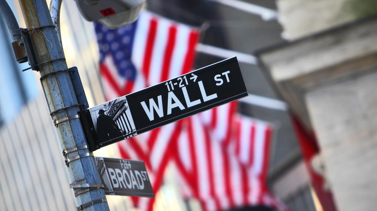 En gatuskylt på Wall Street. Amerikanska flaggor i bakgrunden.