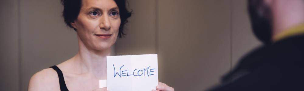 A student stands in front of another person with a sign that says "welcome".