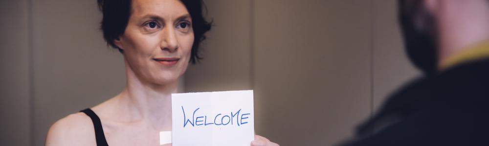 Performance student welcomes audience with a sign that says "welcome"