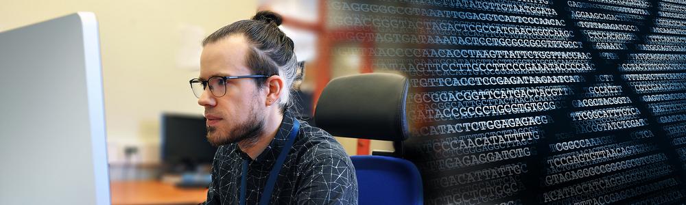 Researcher in front of the computer as well as picture of genome.