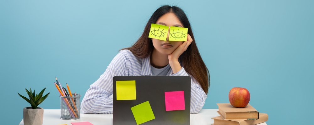 En student sitter vid ett skrivbord. Postitlappar i ansiktet. Stressad.