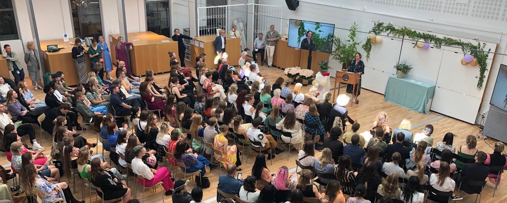 Fotografi av rader med sittande studenter framför talarstol med kvinna som talar.
