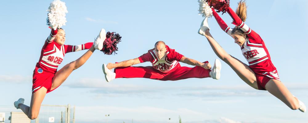 två kvinnliga och en manlig cheerleaders hoppar högt.