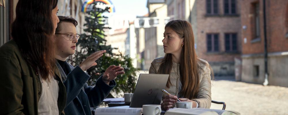 Three students in discussion, at a table full of books and coffee cups
