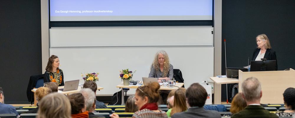 Three people are having a chat in front of an audience sitting in a lecture hall.