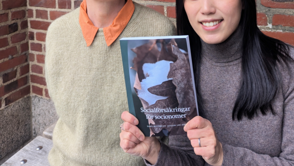 Sara Hultqvist och Jayeon Lee håller upp boken "Socialförsäkringar för socionomer".