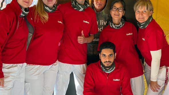 Seven people in red clothing pose in front of preparedness sign inside tent.