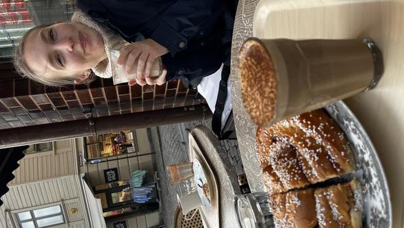 kvinna fikar på kafé och äter stor kanelbulle.