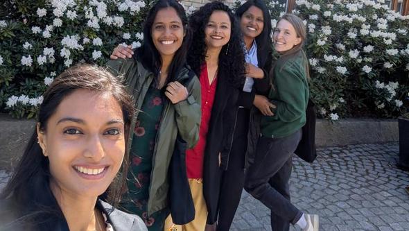 en grupp glada kvinnor framför blommande buskar.